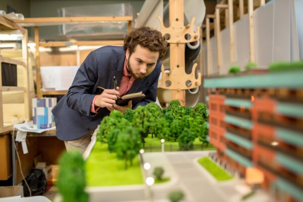 Person inspecting architectural scale model, taking notes